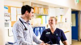 A medium close up shot of a male doctor and female nurse smiling at each other while filling out paper work.