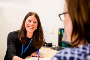 An over the shoulder photo of a woman wearing a lanyard smiling and holding a pen