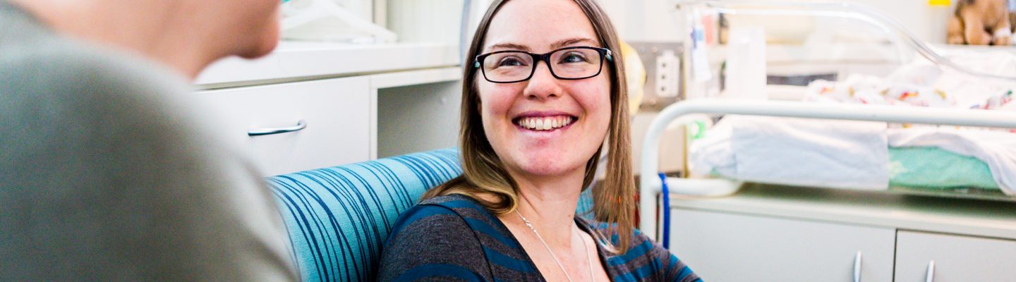A young woman smiles while looking at her partner and holding a baby.