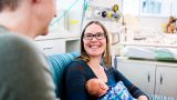 A young woman smiles while looking at her partner and holding a baby.