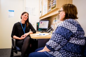 A woman wearing a blue lanyard sits at a desk with a female patient